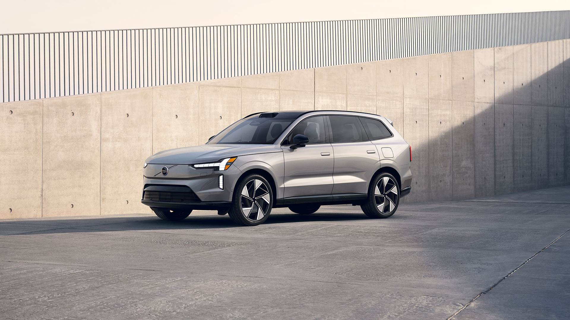 Light silver colored Volvo EX90 in front of cement wall